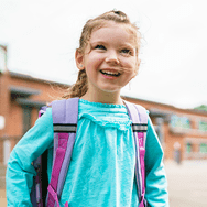 A little girl in a teal shirt standing outside of her school