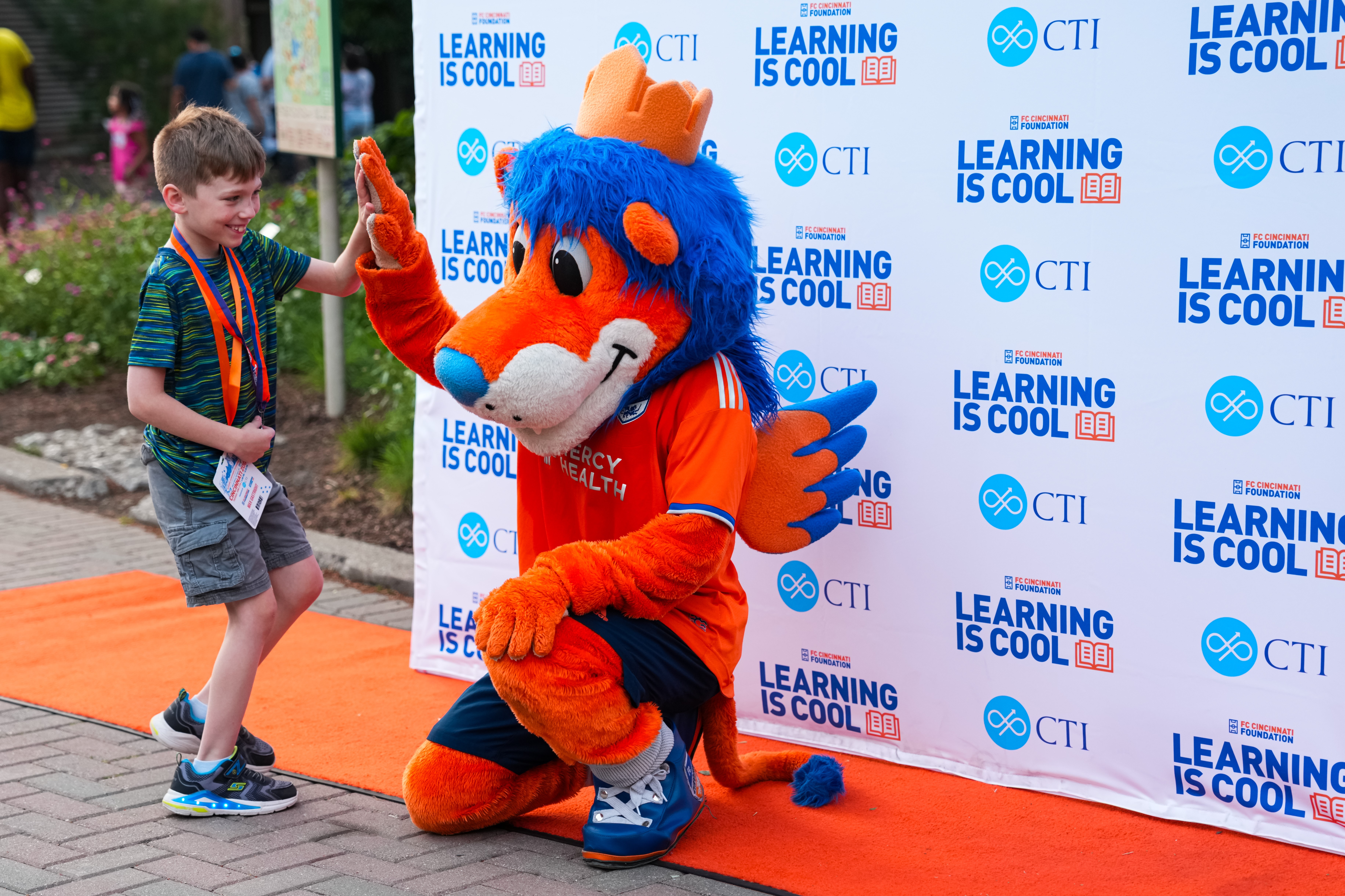 Little boy high fiving Gary the Lion in front of "Learning Is Cool" backdrop