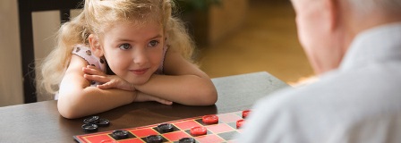 Granddaughter smiling at grandfather while playing checkers