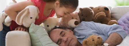 Granddaughter watching over sleeping grandfather surrounded by stuffed animals