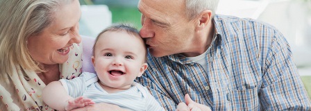 Grandmother smiling at grandchild as grandfather kisses baby's head