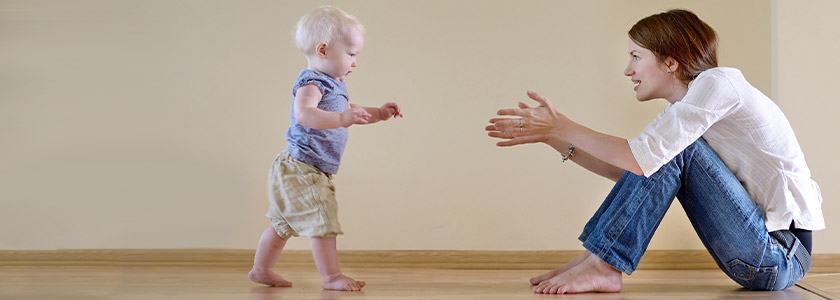Toddler walking to mom who has her arms outstretched
