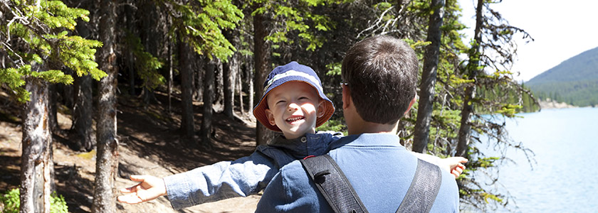 Boy in hat stretches out his arms as he enjoys the sun as his father carries him