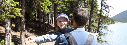 Boy in hat stretches out his arms as he enjoys the sun as his father carries him