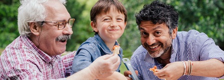 Grandfather, grandson, and son make faces at the camera while eating