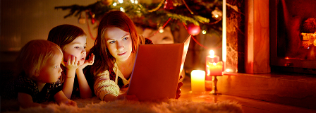 Mom reading to her young son and daughter by the Christmas tree