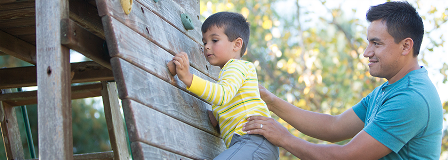 Father holds onto young son as he climbs wall at playground